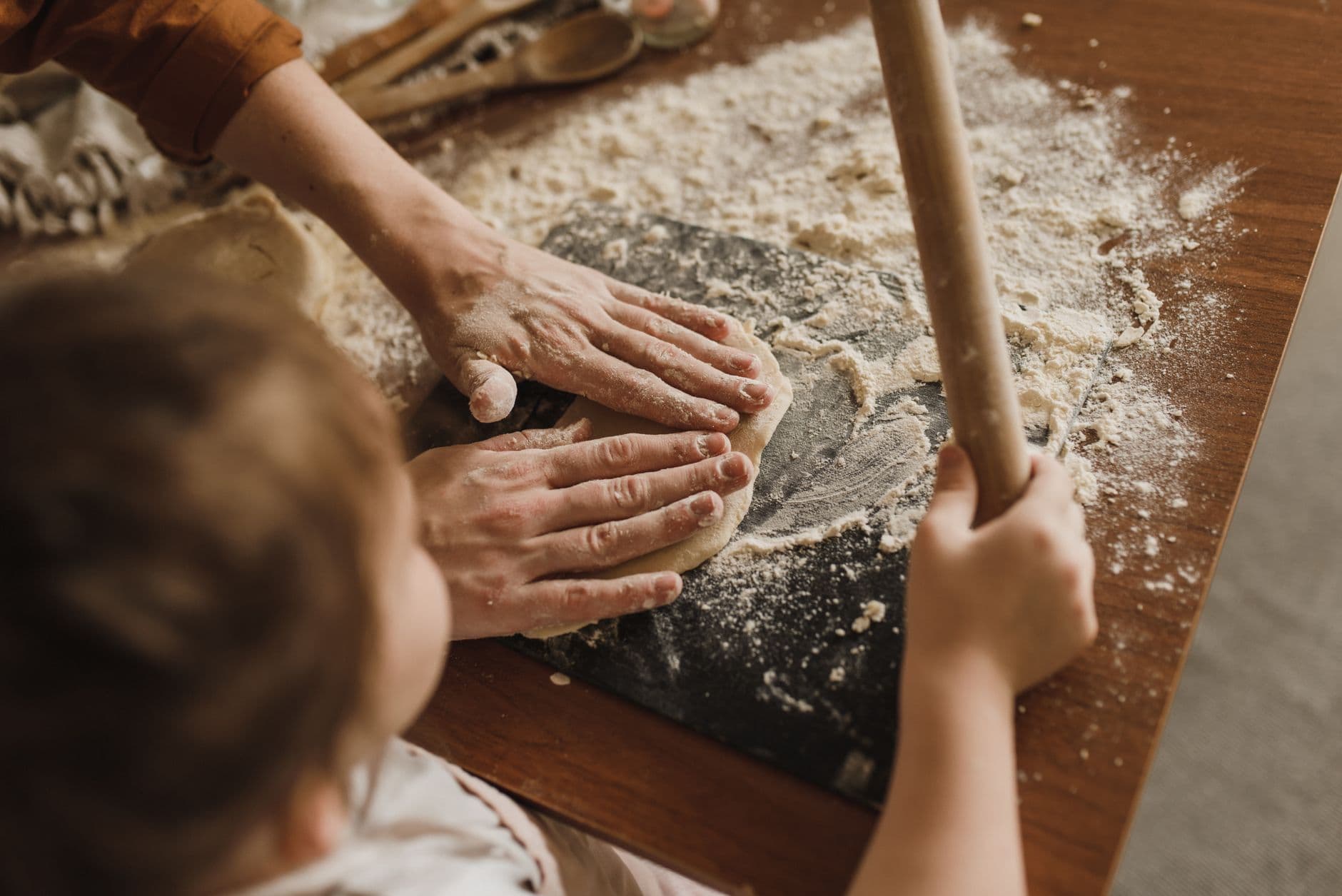 A parent and child kneading bread dough together on a floured table